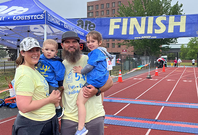 Family of four standing on track with large finish line behind them