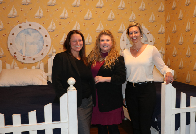 Lauren Ayers, Jennifer Brandt and Dr. Nora Perkins from Albany ENT & Allergy Services stand in the "Safe Harbor" bedroom at the Albany Ronald McDonald House, featuring yellow wallpaper with sailboats