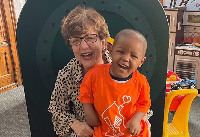 Resident House Director Debbie Ross laughs with a child in an orange t-shirt at the Albany Ronald McDonald House