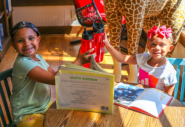 Two young girls clink their READ for RMHC-CR water bottles over a few favorite books at the Albany Ronald McDonald House