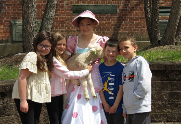 Elementary school students with their principal dressed as Little Bo Peep holding a sheep