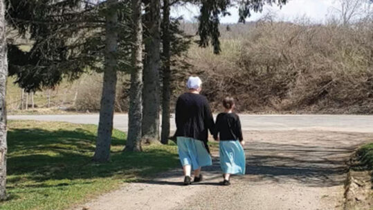 Amish mother and daughter pictured from behind, walking down a dirt road