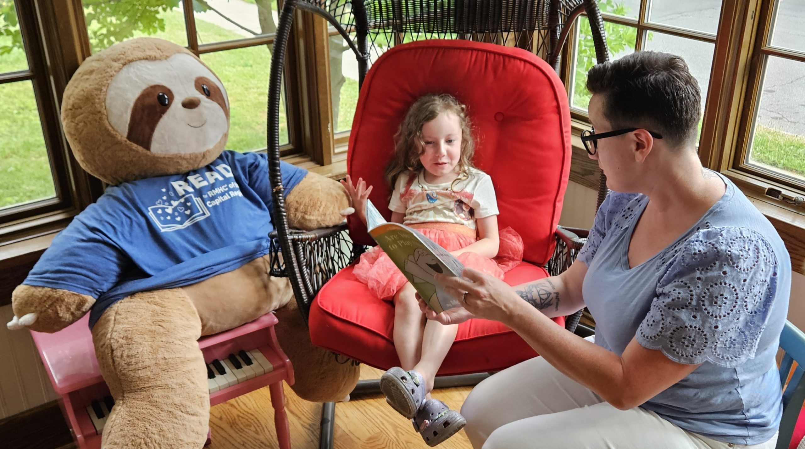young girl reading with her mother next to a stuffed sloth in a READ tee shirt