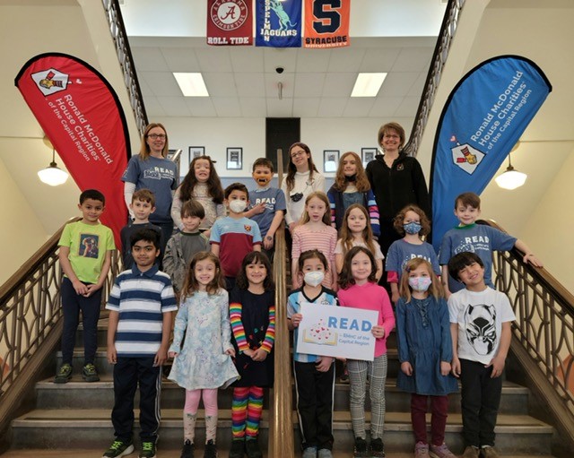 Student readers from New Scotland Elementary School standing on steps with READ for RMHC-CR poster and flags