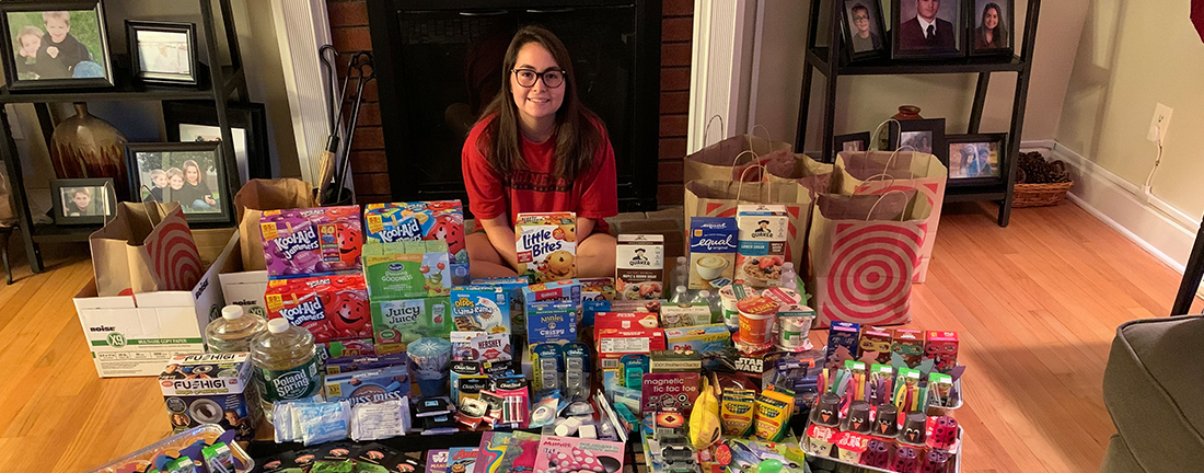 Teen volunteer poses with a large collection of wish list donations for Ronald McDonald House Charities of the Capital Region