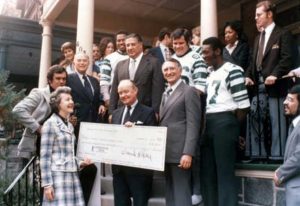 Large group stands in front of house with big check